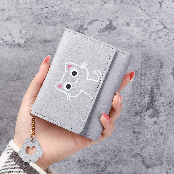 Hand holding gray wallet with cute white cat design and flower charm on chain