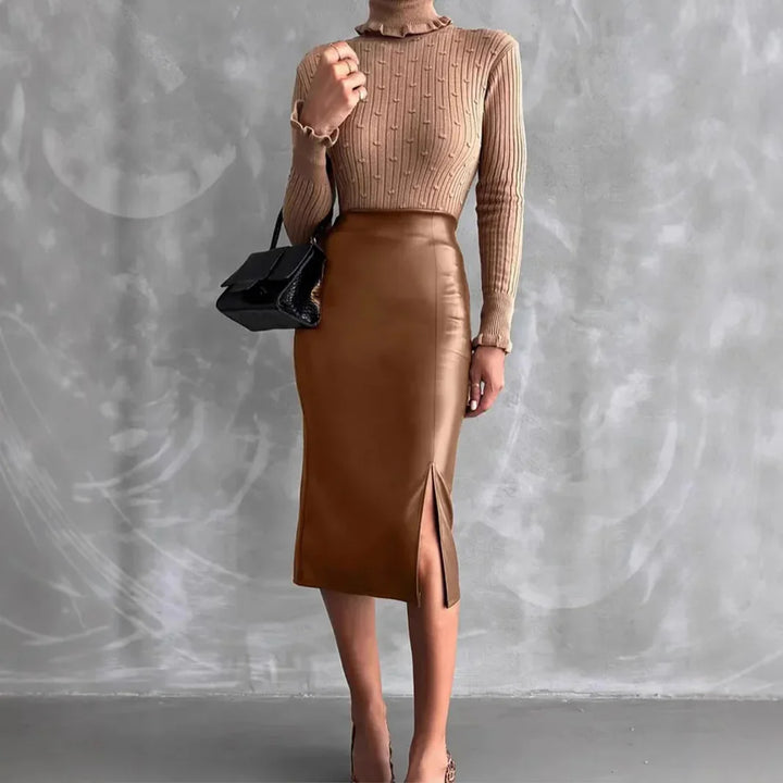 Woman wearing beige textured turtleneck sweater and brown leather midi skirt with front slit holding black handbag