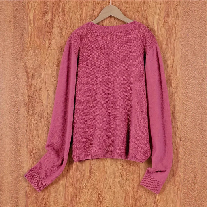 Soft pink knit sweater hanging on wooden hanger against wood panel background