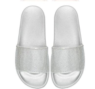 Silver slip-on slides with wide straps covered in rhinestones on white background
