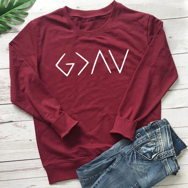 Maroon crewneck sweatshirt with white 'G>AV' graphic text laid on white wood background next to folded blue jeans