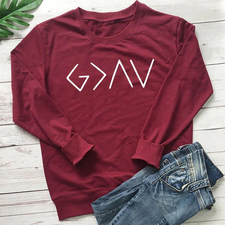 Maroon crewneck sweatshirt with white 'G>AV' graphic text laid on white wood background next to folded blue jeans