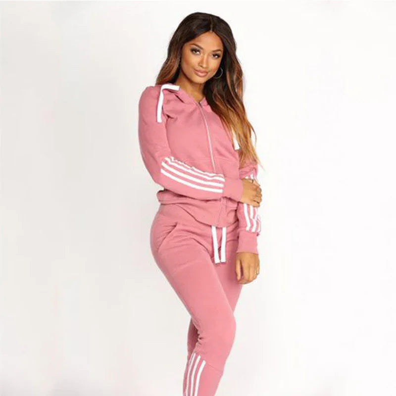 Woman wearing pink tracksuit with white stripes on sleeves and pants, posing against white background