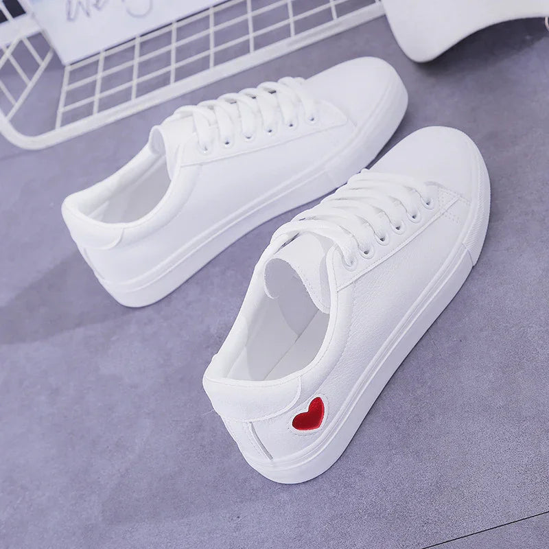 White casual sneakers with red heart detail on side, set on gray floor with metal grid background