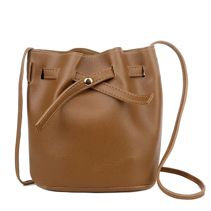 Brown leather bucket bag with adjustable strap and drawstring closure on white background