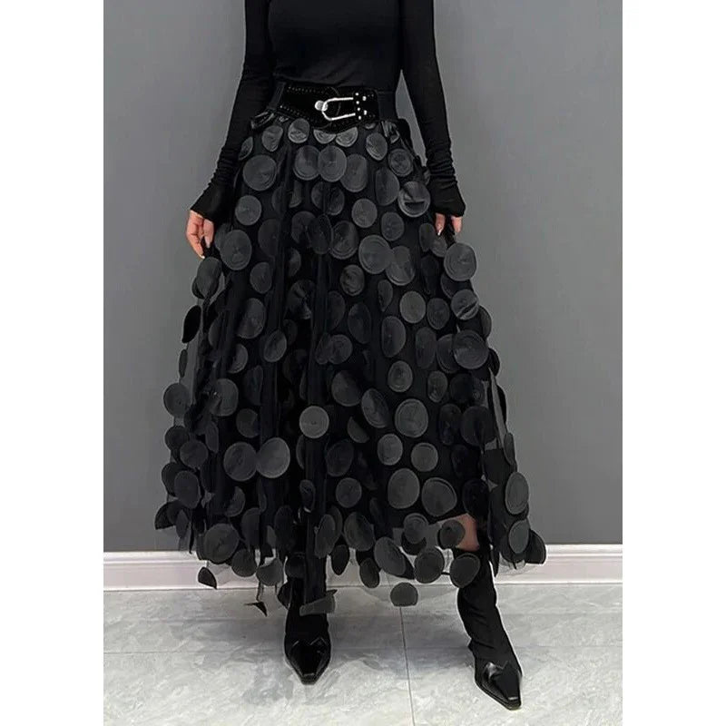 Woman wearing black maxi skirt with large circular appliques, black top, belt, and pointed black boots