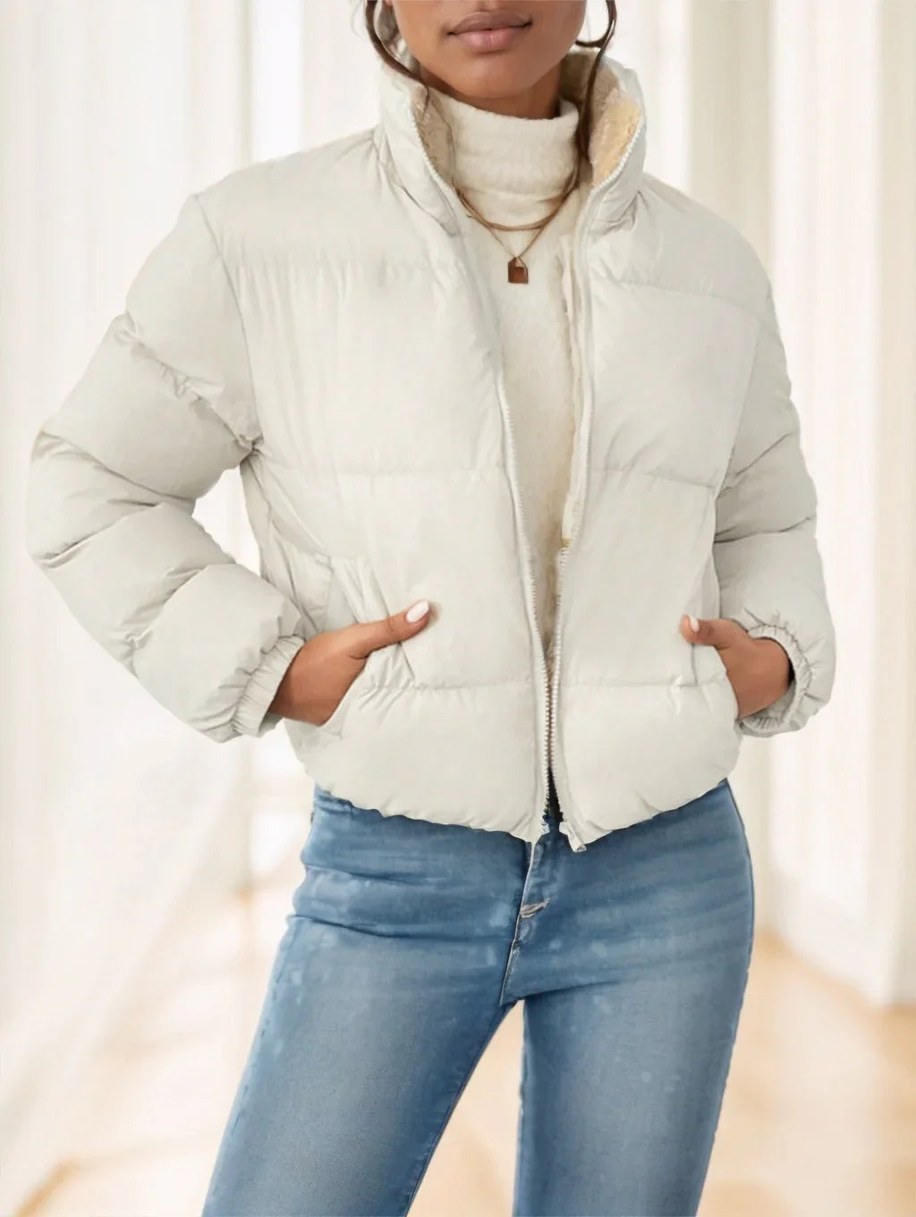 Woman wearing a cream puffer jacket over a white turtleneck sweater and blue jeans