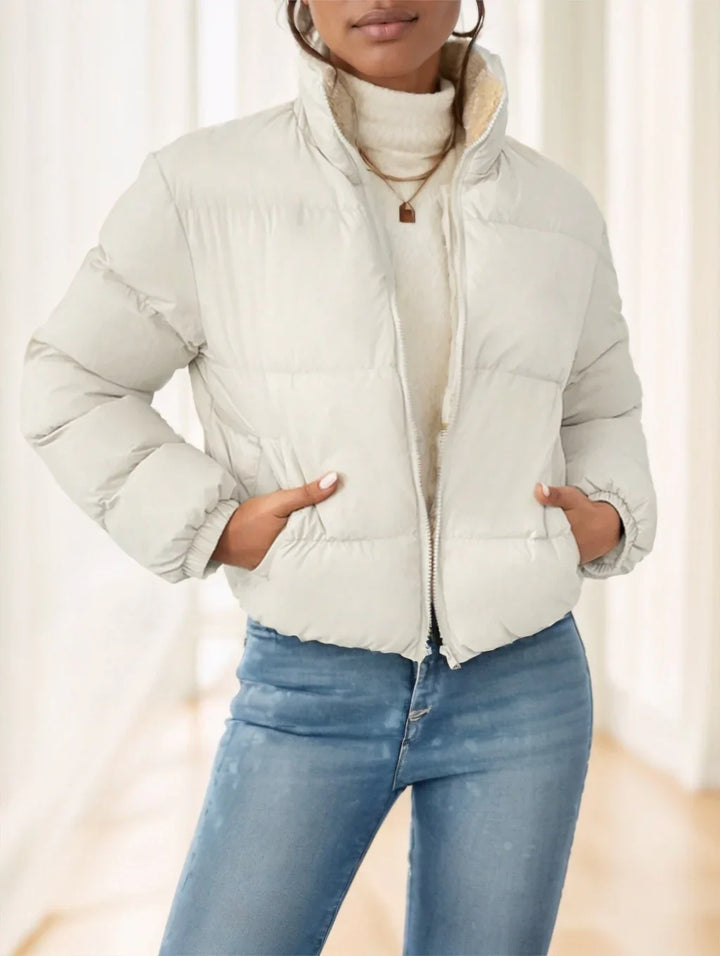 Woman wearing a cream puffer jacket over a white turtleneck sweater and blue jeans