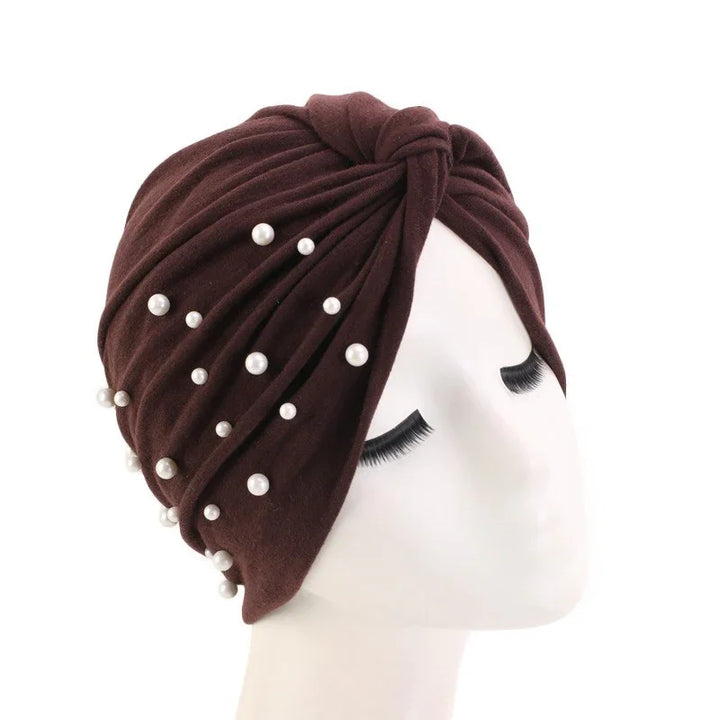 Brown turban headwrap adorned with scattered pearl beads on mannequin head with long eyelashes