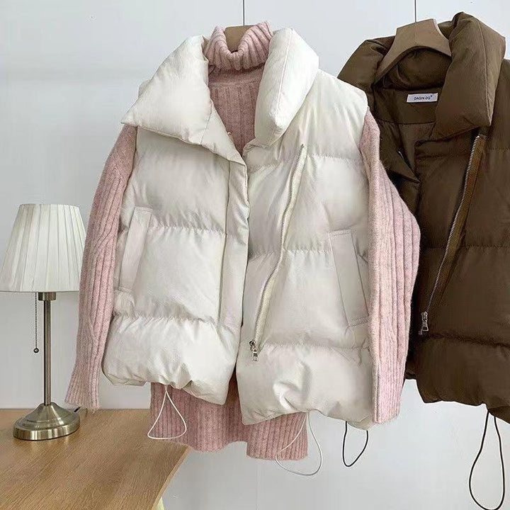 White and brown puffer vests with pink ribbed turtleneck sweater on wooden hangers by table lamp