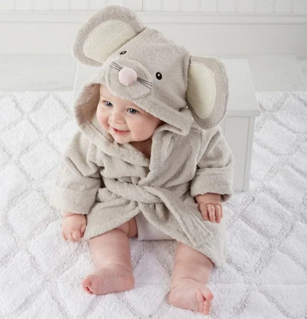 Baby wearing a soft gray mouse-themed hooded bathrobe sitting on a white textured carpet in a bright room