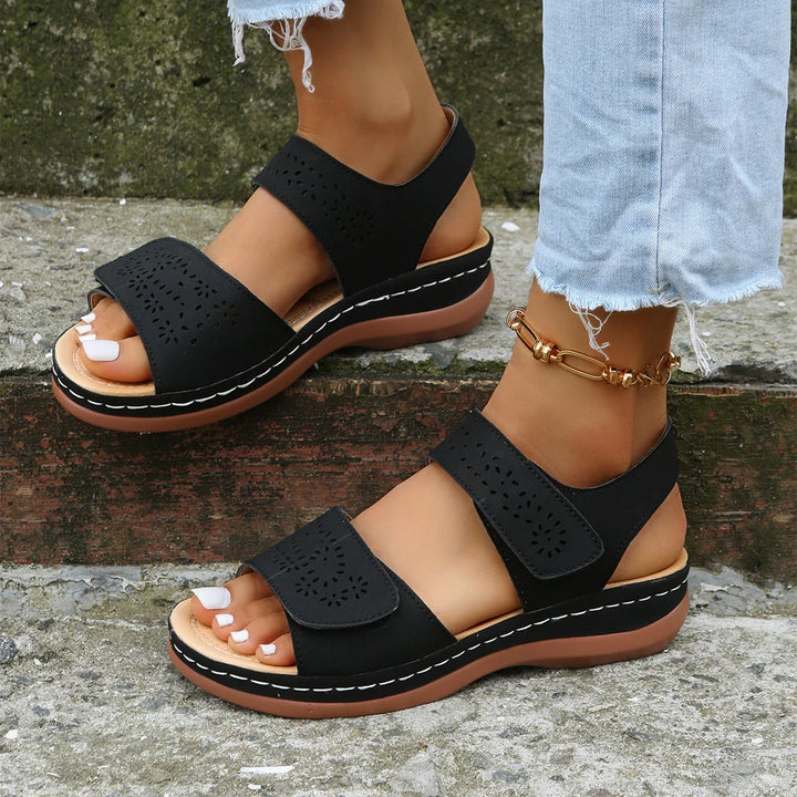 Black casual sandals with floral cutout design worn with light-wash frayed jeans and gold anklet