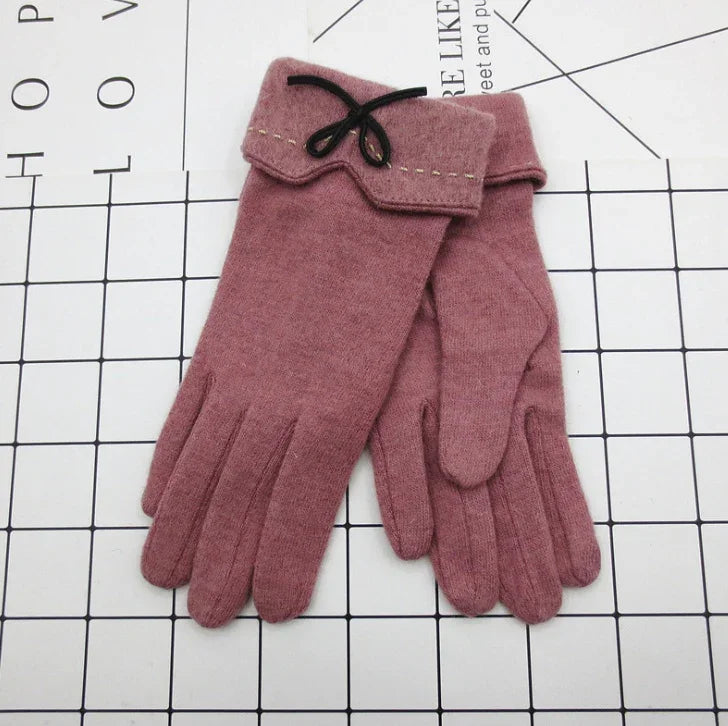 soft pink women's wool gloves with decorative black bow and stitched cuffs on grid surface