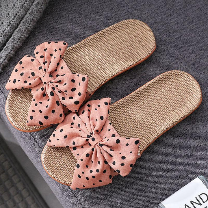 Pink polka dot bow slippers with woven straw footbed on gray fabric surface
