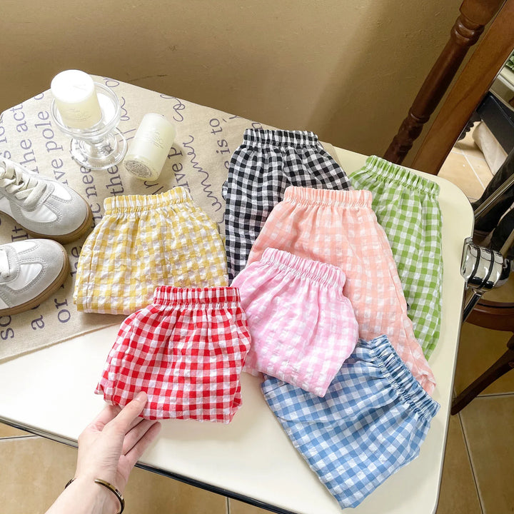 Collection of colorful gingham checkered elastic waist shorts in red, yellow, pink, blue, green, black, and peach on white table