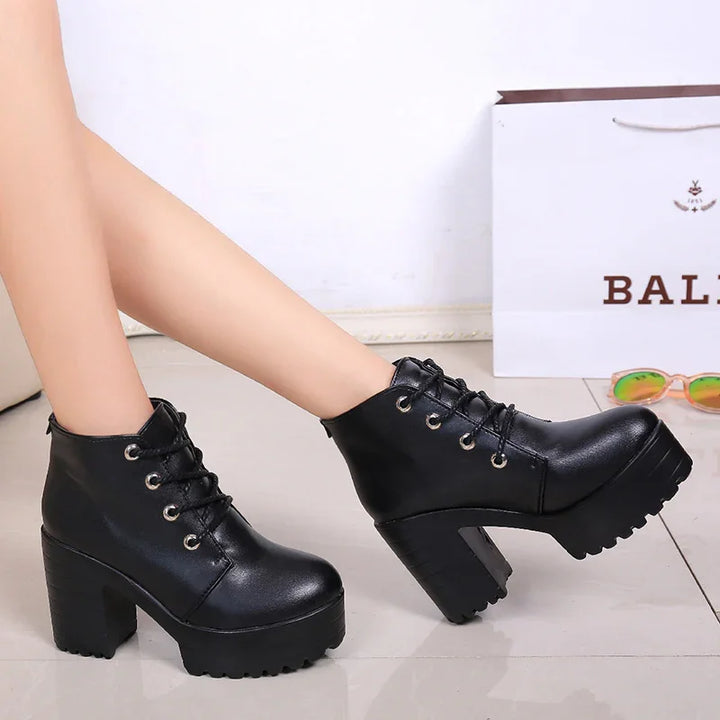 Black chunky platform lace-up ankle boots worn on tiled floor with shopping bag and sunglasses in background