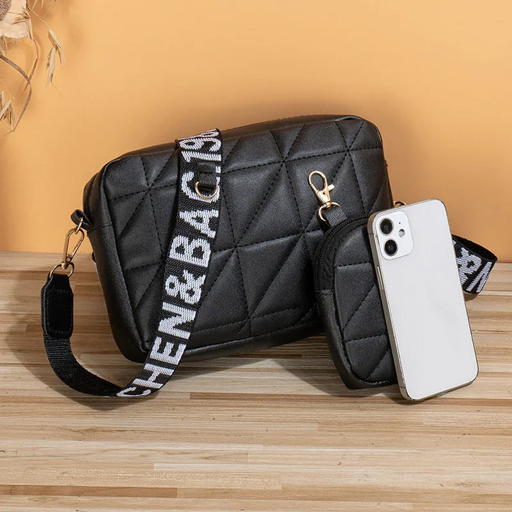 Black quilted crossbody bag and matching pouch with white smartphone on wooden surface