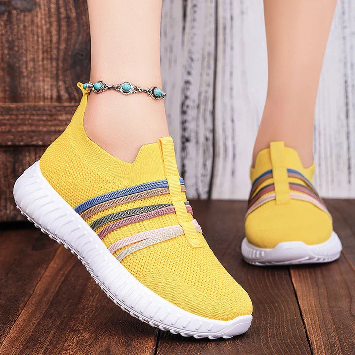 Yellow knit slip-on sneakers with multicolor stripes and white soles on wooden floor