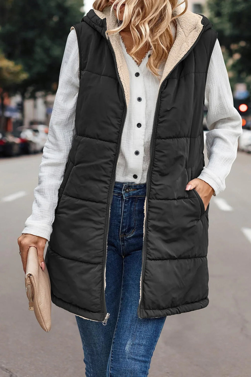 Woman wearing black quilted sleeveless hooded vest with white fleece lining over white button-up shirt and blue jeans