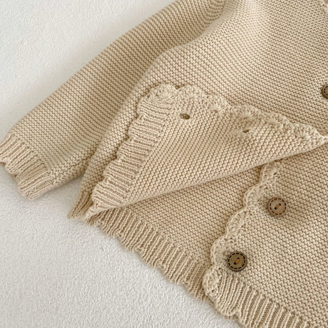 Close-up of beige knitted cardigan with scalloped edges and wooden buttons on white background