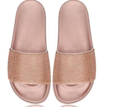 Pair of rose gold slide sandals with textured sparkling straps on white background