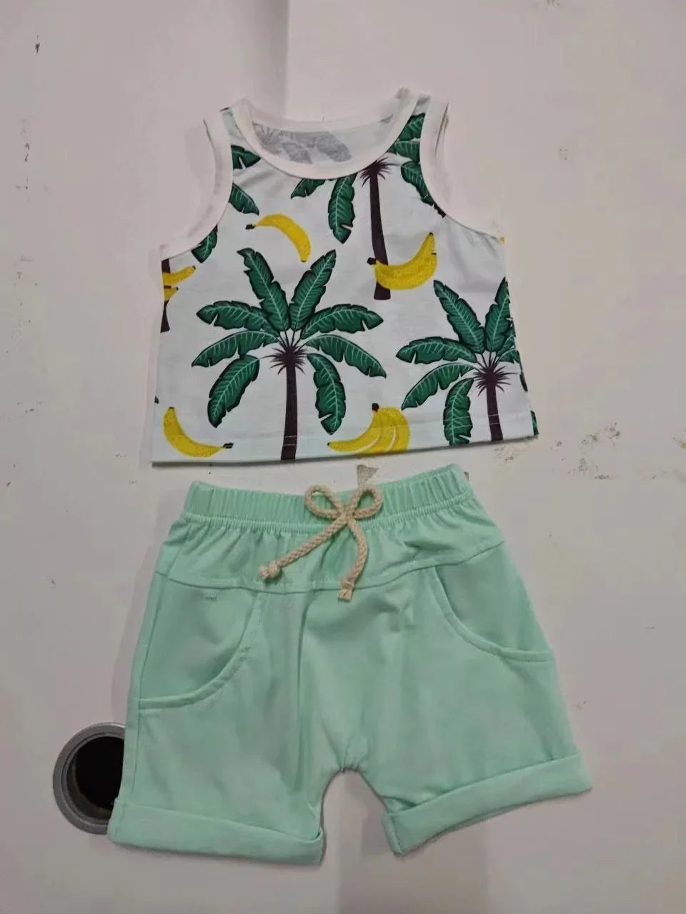 Baby summer outfit with white tank top featuring green palm trees and yellow bananas, paired with light green shorts