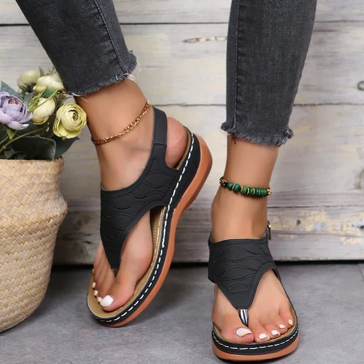 Women's black open-toe sandals with thick brown soles, worn with dark gray jeans and ankle bracelets