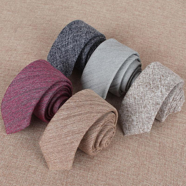 Five rolled textured men's neckties in burgundy, navy blue, light gray, beige, and brown on a woven fabric background