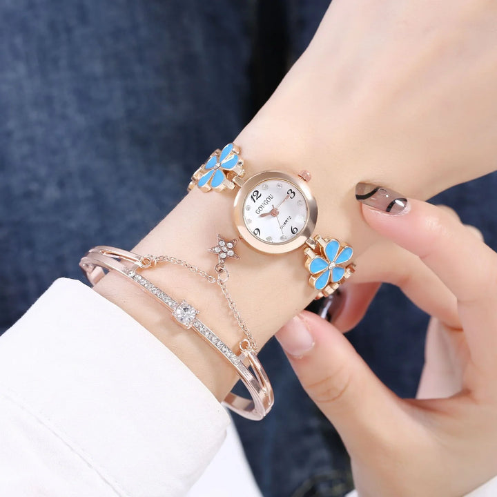 Close-up of a wrist wearing a gold watch with blue butterfly accents and a rhinestone bracelet