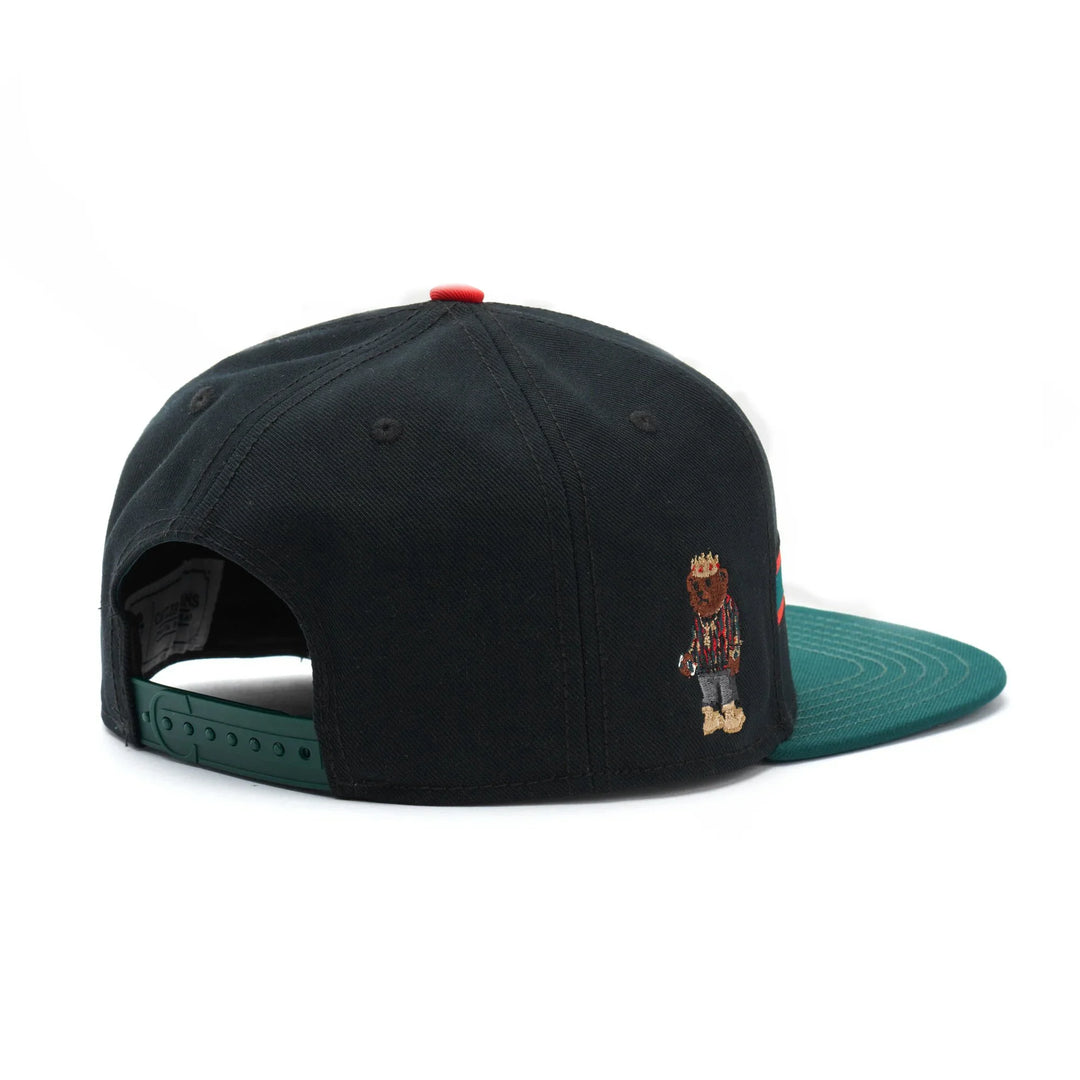 Black snapback hat with green brim and embroidered bear wearing crown and striped shirt on side