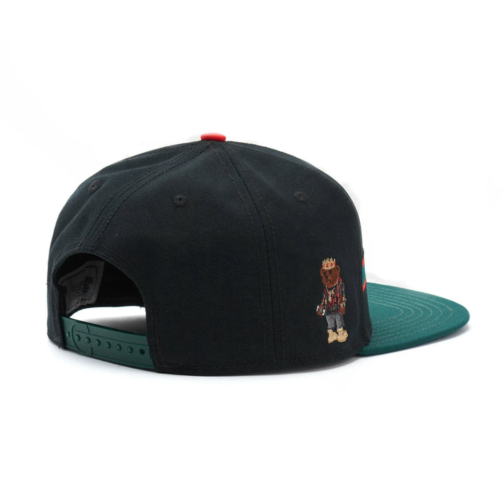 Black snapback hat with green brim and embroidered bear wearing crown and striped shirt on side