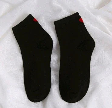 Pair of black ankle socks with small red heart detail on white fabric background