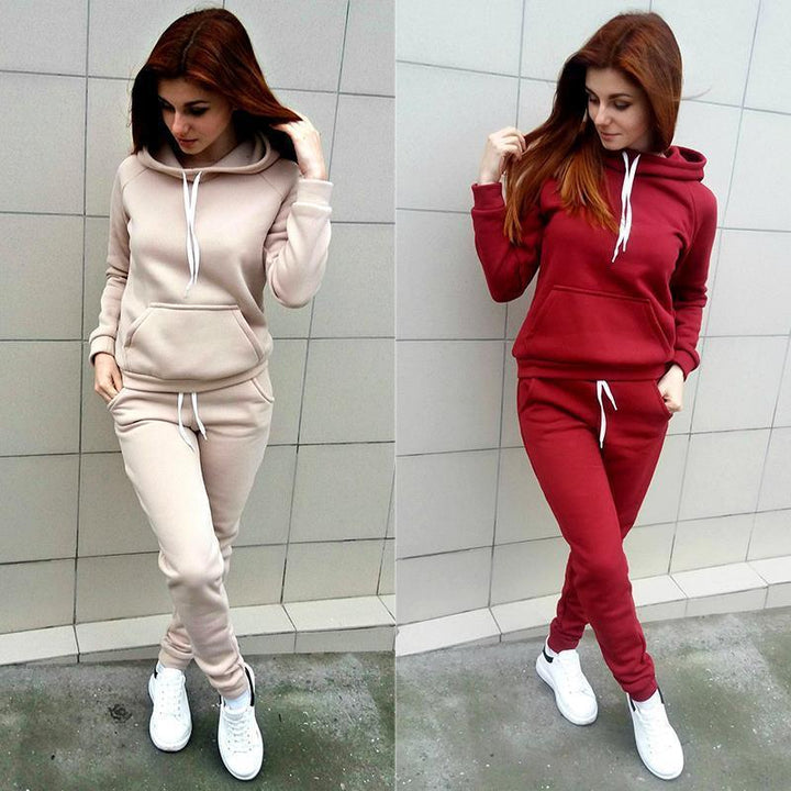 Woman wearing matching beige and red hooded tracksuits with white sneakers against a tiled wall