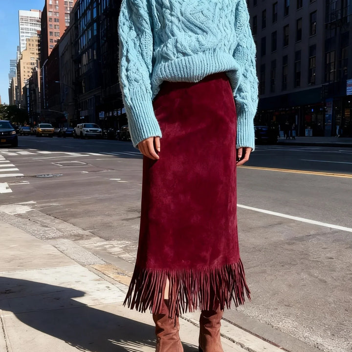 Woman wearing a light blue cable knit sweater and burgundy suede fringe skirt on city street