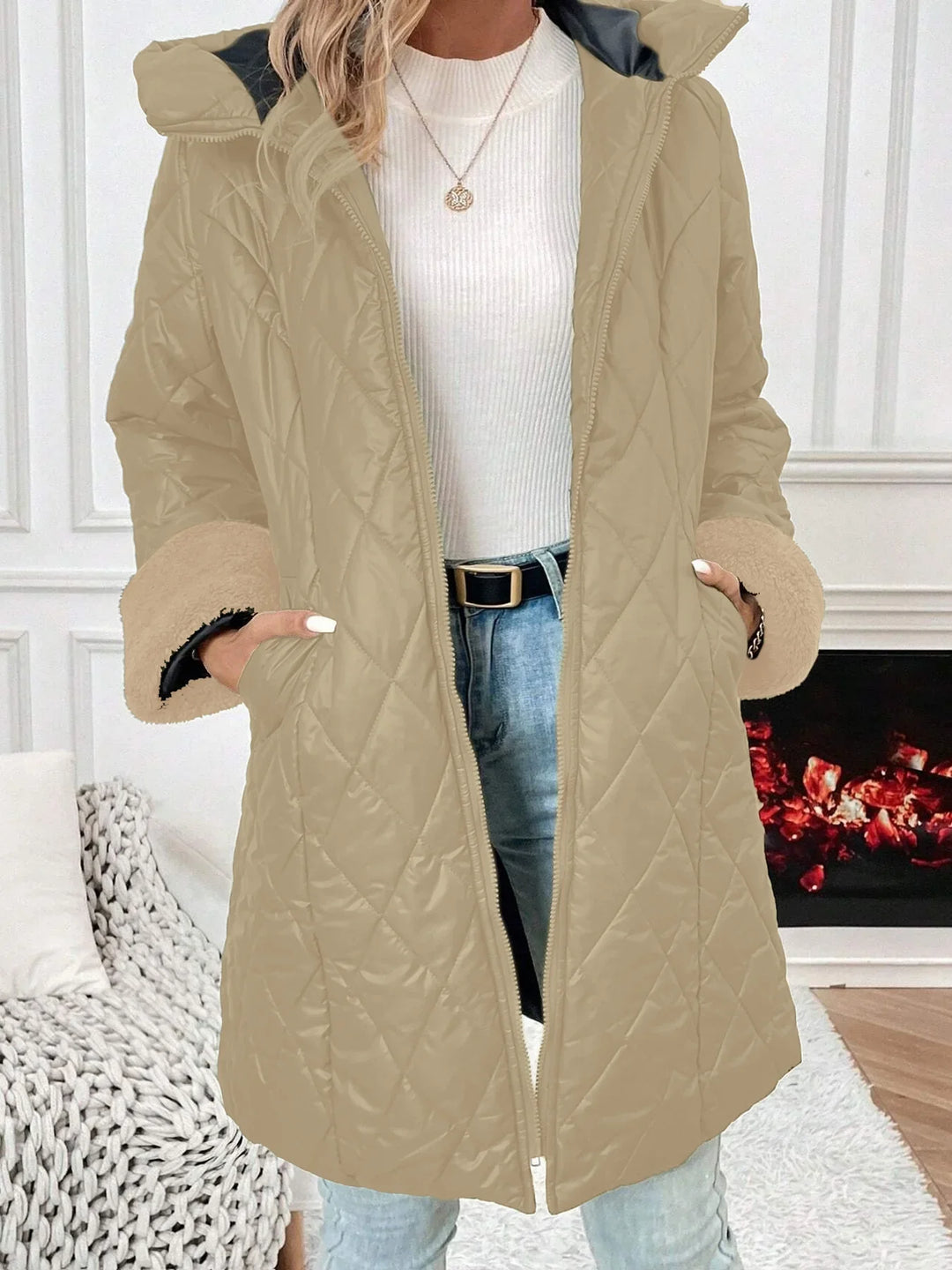 Woman wearing beige quilted winter coat with fur cuffs over white ribbed sweater and light blue jeans