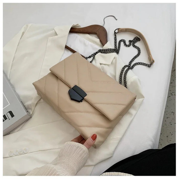 Beige quilted leather crossbody bag with black clasp and chain strap on white blazer