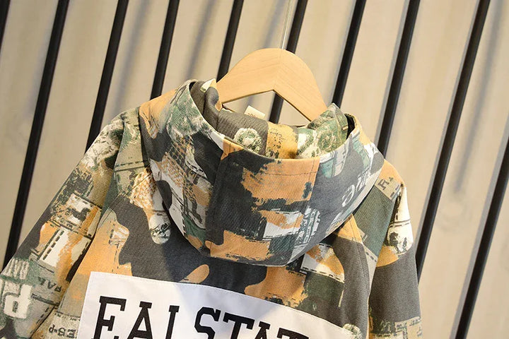 Camouflage print hoodie with abstract beige, green, and black patterns hanging on wooden hanger