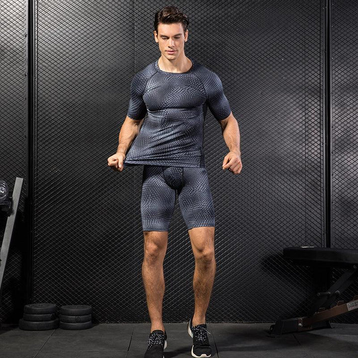 Man wearing black compression athletic set in gym with textured wall and fitness equipment