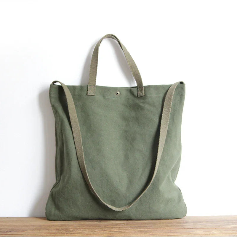 green canvas tote bag with short handles and long shoulder strap on wooden surface
