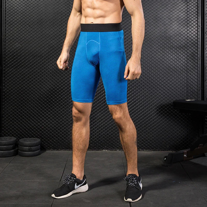 Man wearing blue compression shorts and black sneakers in gym with mesh wall background