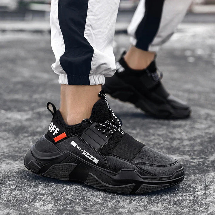 Black chunky sneakers with white 'keep running' text, worn with black and white track pants on asphalt