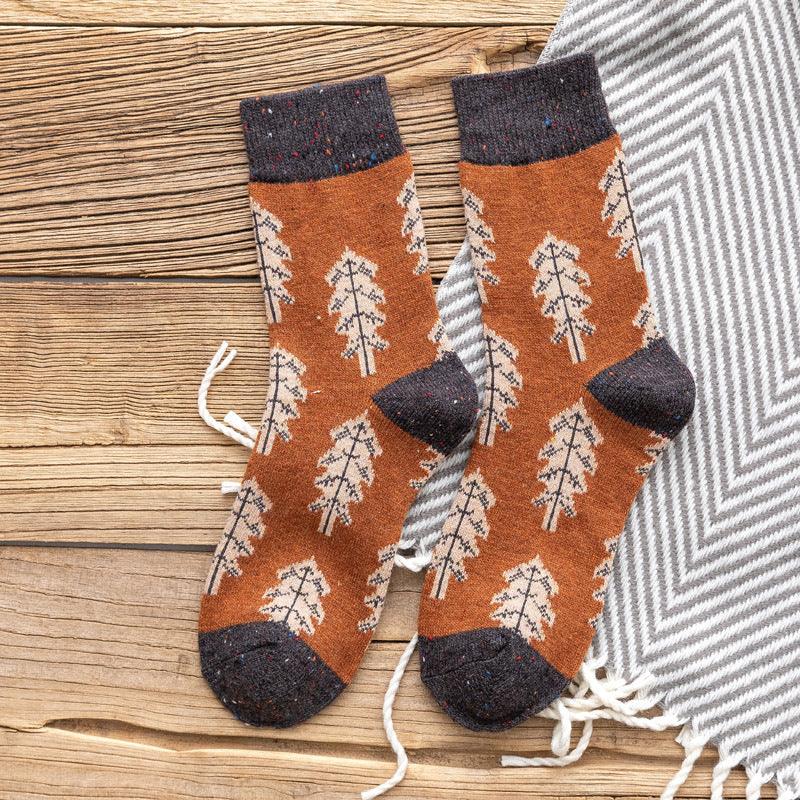 Brown wool socks with beige leaf pattern and dark gray cuffs, heels, and toes on wooden surface with gray patterned fabric