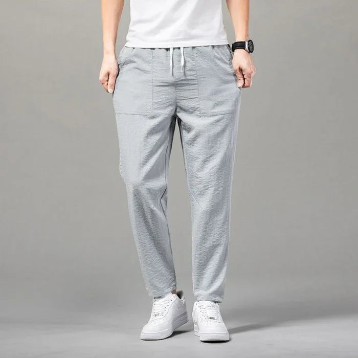 Man wearing light gray casual drawstring pants and white sneakers on plain gray background