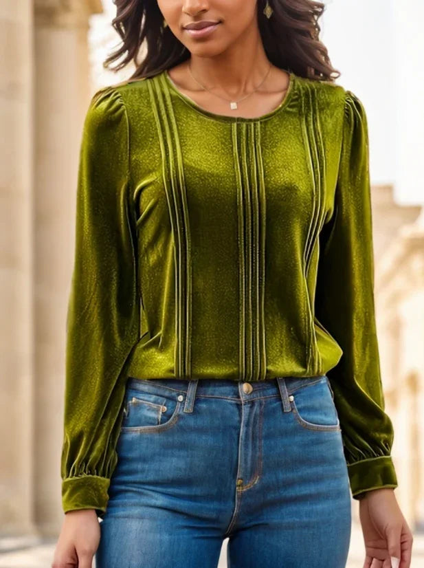 Woman wearing olive green velvet blouse with vertical pleats and puffed sleeves paired with blue jeans