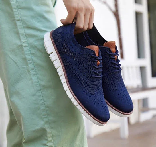 Hand holding navy blue knit casual shoes with white soles against light green pants background