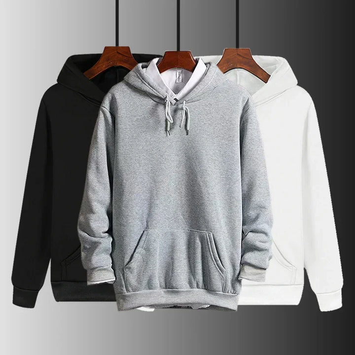 Three plain hoodies in black, gray with white shirt underneath, and white on wooden hangers