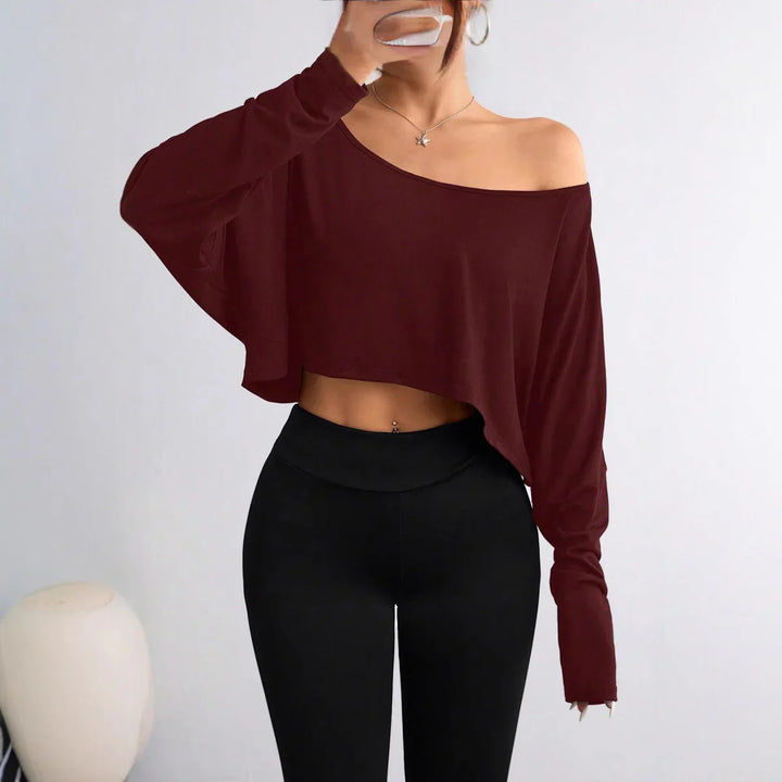 Woman wearing burgundy off-shoulder cropped sweater with black leggings, holding phone for selfie
