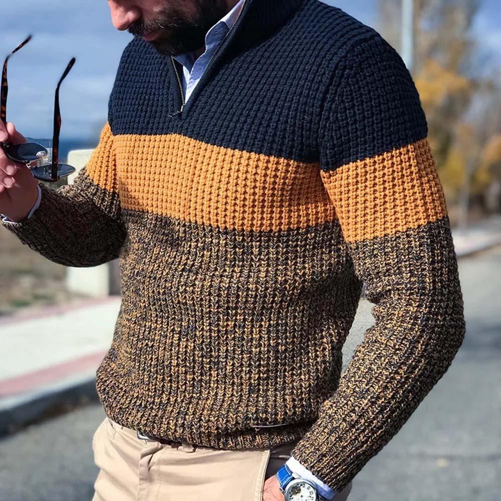 Man wearing a textured knit sweater with navy, mustard, and brown color blocks, holding sunglasses outdoors