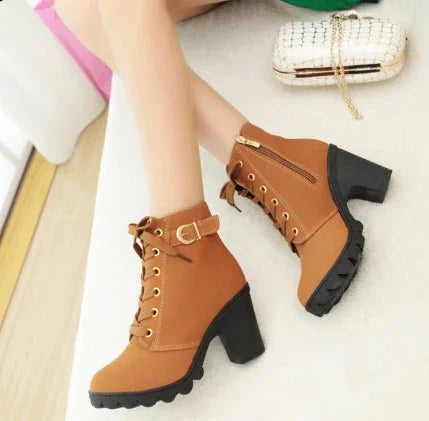 Brown lace-up ankle boots with block heels and side zippers worn by a person sitting on a light surface