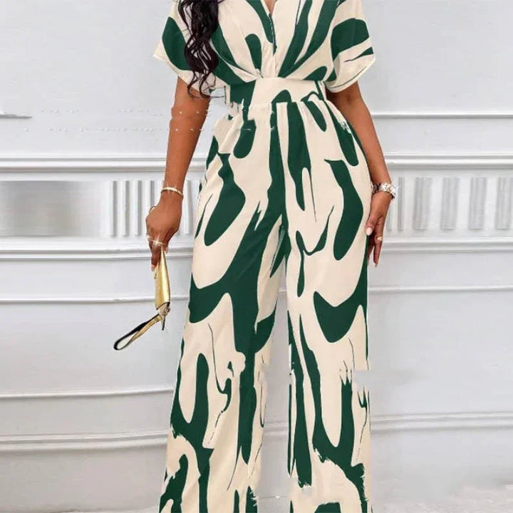 Woman wearing a cream and dark green abstract patterned wide-leg jumpsuit holding a gold clutch